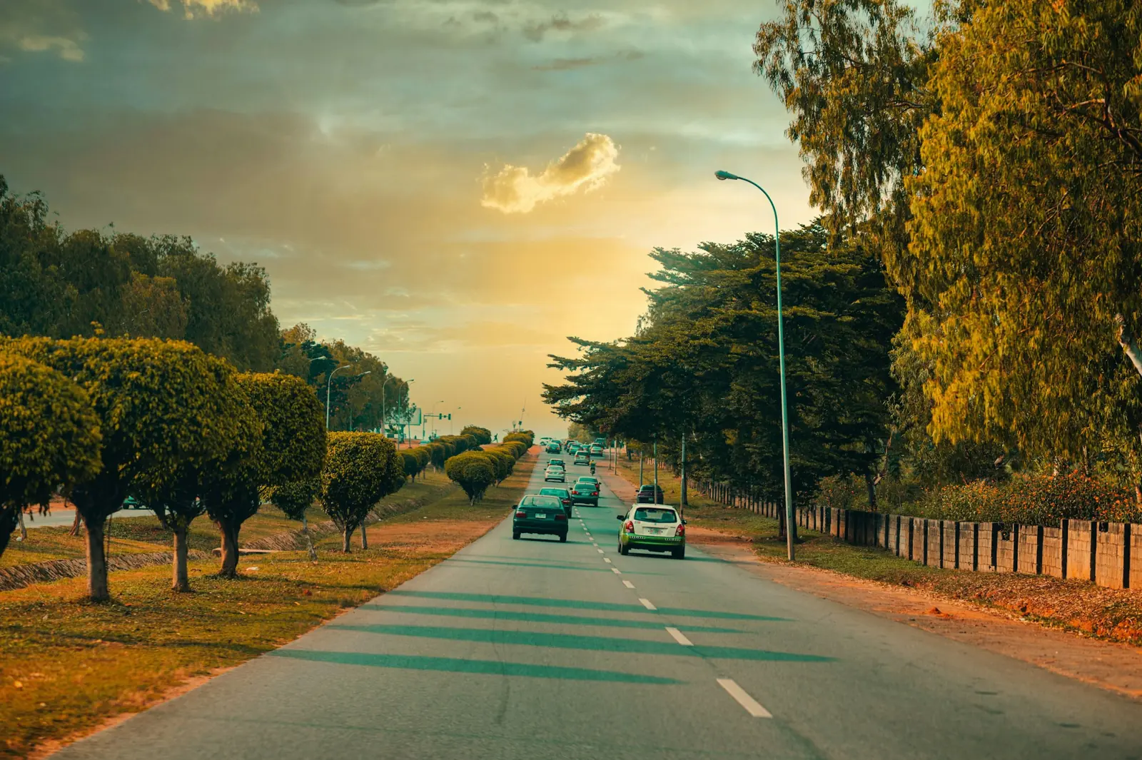 A wide tree-lined Abuja road at golden hour