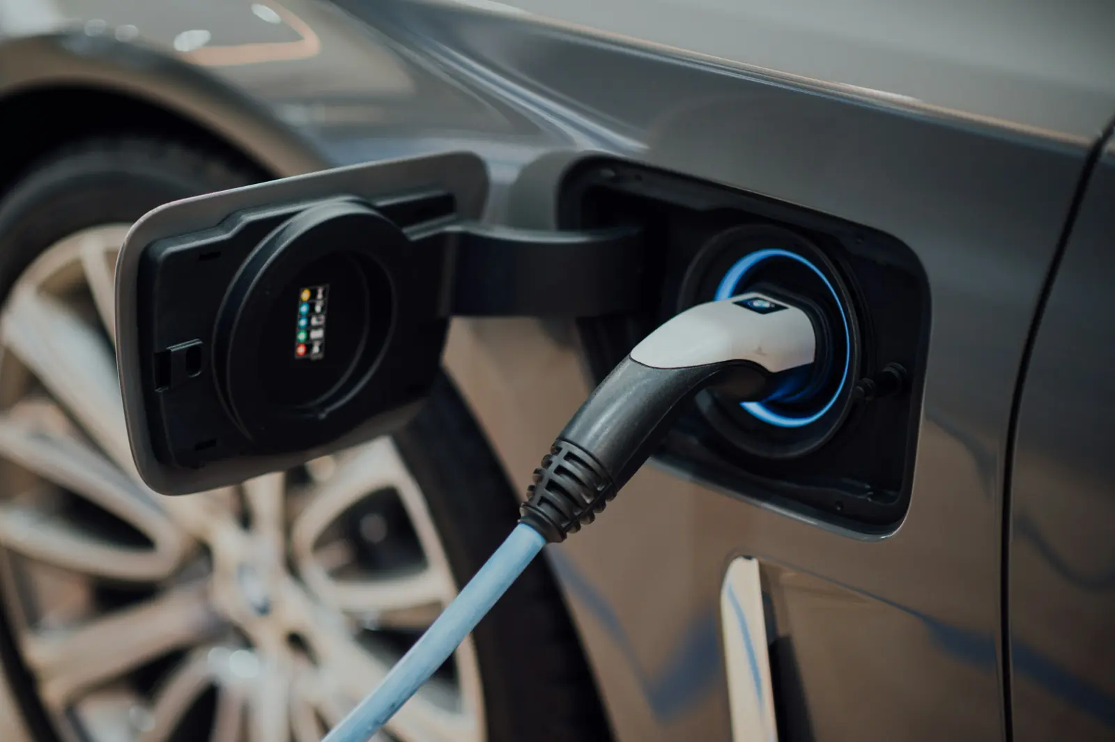 A charging cable plugged into an electric car's charge port, lit blue